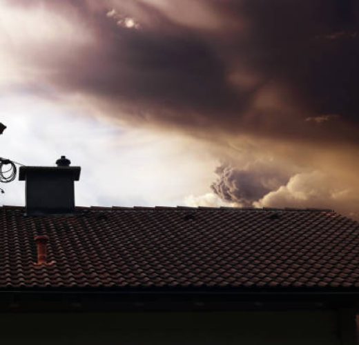 A chimney sweep cleans the chimney on a house roof while thunderclouds gather